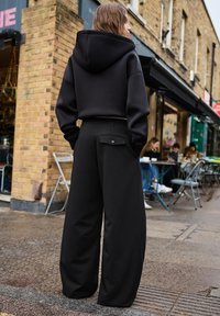 Black oversized hoodie with a hood and relaxed fit, paired with high-waisted black wide-leg trousers featuring back pocket detail.