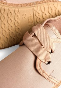 Scarpe in tela beige con una suola testurizzata e flessibile. Presentano una fascia larga con bande elastiche e occhielli in metallo per una chiusura sicura.