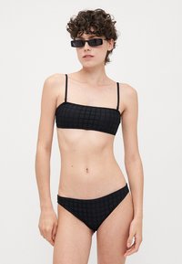 Black bikini set featuring a textured bandeau top with thin straps and matching low-rise bottoms. Material appears lightweight and stretchy.
