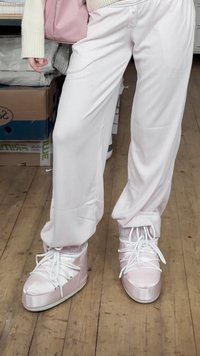 Zapatillas altas de satén rosa con cordones blancos y suela gruesa. Combinadas con pantalones blancos de corte ancho. Suelo de madera al fondo.