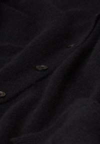 Schwarzer Strickpullover aus weichem Stoff mit drei runden Knöpfen an der Vorderseite. Die Textur wirkt plüschig und leicht dehnbar.
