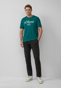 Miętowa koszulka z krótkim rękawem z białym napisem, zestawiona z ciemnymi spodniami i białymi trampkami. Prosty design bez wzorów czy zauważalnych akcentów.