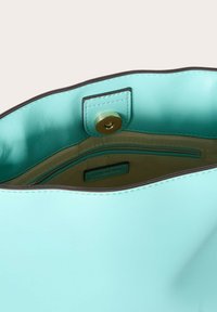 Interno di una borsa in pelle verde menta con una texture liscia, dotato di una tasca con zip e una chiusura a scatto magnetica. Cuciture a contrasto visibili.