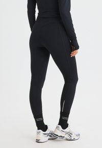 Black leggings with a high waistband and smooth texture, paired with white athletic shoes featuring black accents and reflective details.
