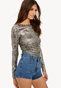 Top long-sleeve en sequins argentés avec une coupe ajustée, associé à un short en denim taille haute de couleur bleu clair avec des bords effilochés.