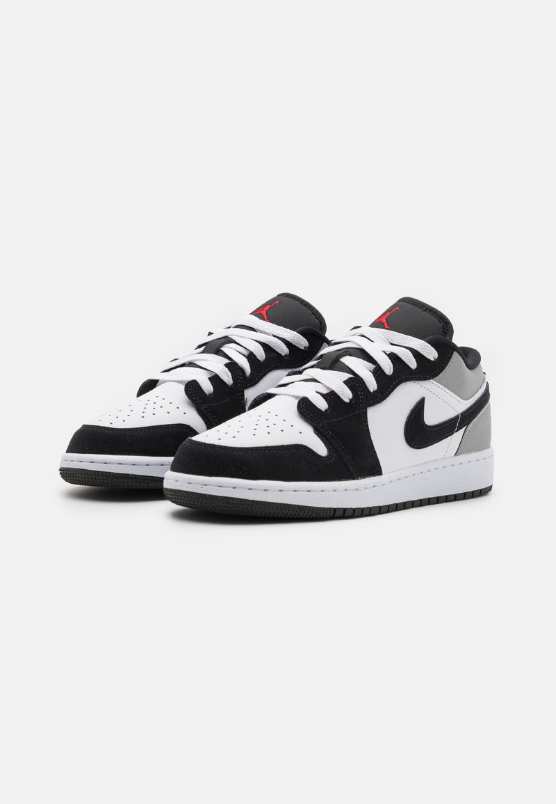Baskets noires et blanches à lacets bas avec des accents gris, possédant un bout perforé, des lacets blancs et une semelle en caoutchouc noire. Logo emblématique sur la languette.