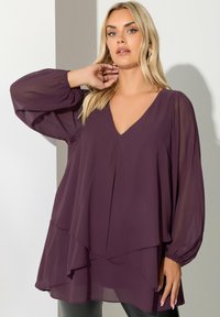 Blusa a maniche lunghe color prugna in tessuto leggero con scollo a V e orlo a strati. Presenta maniche a palloncino arricciate e una vestibilità ampia.
