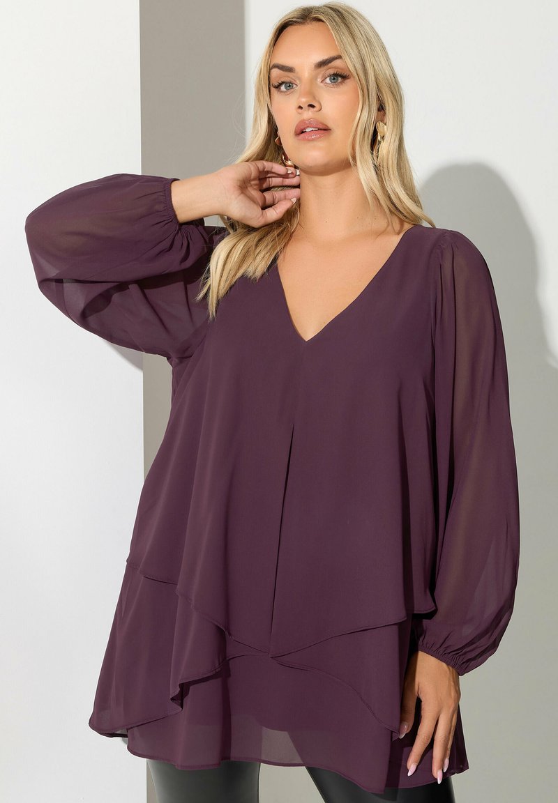 Blusa a maniche lunghe color prugna in tessuto leggero con scollo a V e orlo a strati. Presenta maniche a palloncino arricciate e una vestibilità ampia.