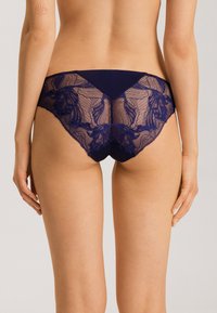 Bragas de encaje de color navy con un panel trasero transparente que presenta patrones florales, junto con una cinturilla opaca y aberturas para las piernas sólidas.