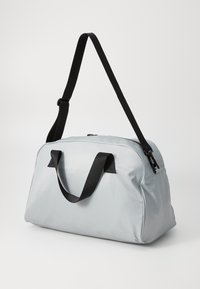 Lys grå duffelbag med sorte håndtag og skulderrem, glat tekstur, lynlåslukning og afrundet rektangulær form.