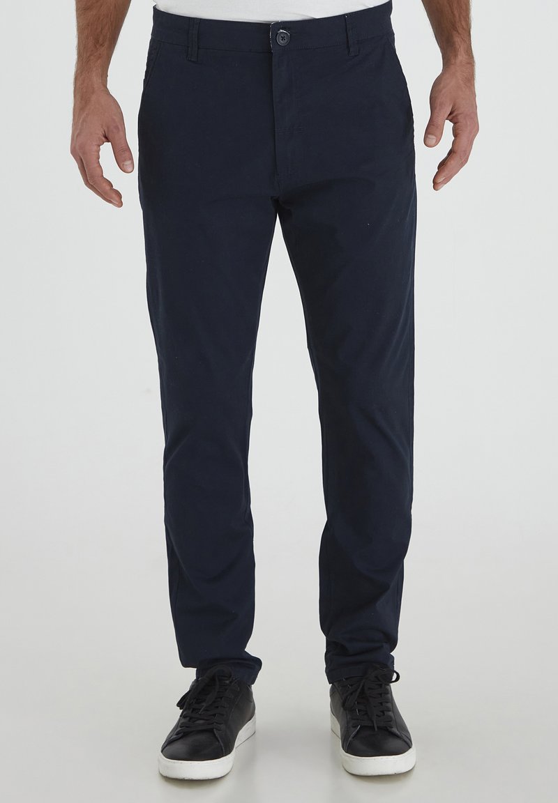 Chino en coton marine à coupe slim, avec poches avant, fermeture à bouton et texture lisse. Associé avec des chaussures de sport noires.
