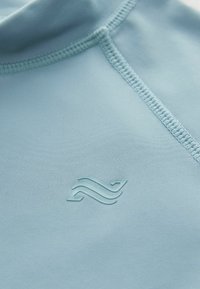 Ljusblå sporttröja i mjukt material, med en upphöjd logotyp och platta sömmar för hållbarhet. Sömmlös kragsdesign.