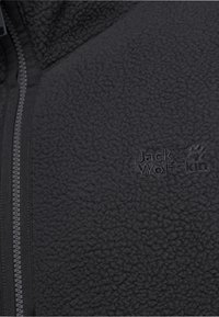Giacca in pile nero con superficie testurizzata, dotata di una zip e del logo "Jack Wolfskin" ricamato con filo scuro.