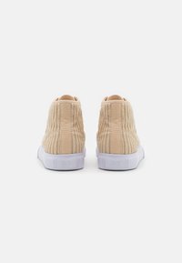 Beige High-Top-Sneaker mit einem strukturierten Textil-Obermaterial und einer weißen Gummisohle. Mit vertikalen Rippdetails an den Seiten und hinten.