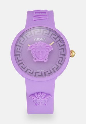 Reloj de silicona púrpura con una cabeza de Medusa en la esfera y en la correa. Patrón de clave griega alrededor de la esfera con manecillas doradas y una corona adornada.