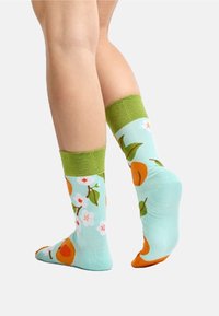 Lichtblauwe sokken met groene boorden, versierd met oranje en bloempatronen. Gemaakt van zachte stof met een gladde textuur, ontworpen voor comfort.