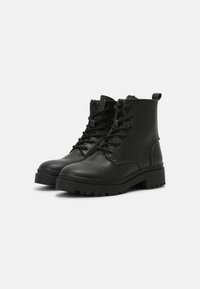Botas de cuero negras hasta el tobillo con punta redondeada, frente con cordones, cuello acolchado y suela resistente. Cuenta con una lengüeta en la parte posterior.