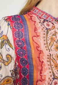Chemise en tissu multicolore présentant des motifs floraux et cachemire complexes. Comprend des rayures audacieuses en rose, rouge et orange avec des accents de fil métallique.