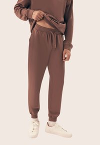 Brązowe, luźne dresy z elastycznym pasem i ściągaczami przy nogawkach. Wykonane z miękkiego materiału, zestawione z białymi trampkami.