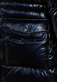Navy blue puffy jacket featuring a glossy, quilted texture with a front pocket and a metallic snap closure.