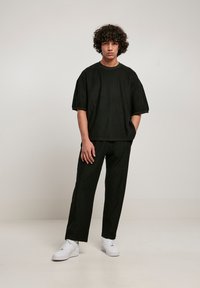 T-shirt negru supradimensionat cu textură fibrată și mâneci scurte, asortat cu pantaloni negri și adidași albi. Stil minimalist.