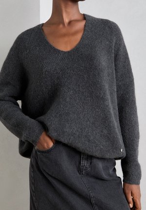 Person wearing a soft, dark gray fuzzy sweater with a V-neck, paired with a high-waisted dark gray denim skirt, posing with one hand in pocket.