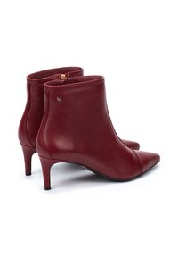 Botas de tobillo de cuero rojo con punta afilada, tacón bajo y cierre de cremallera en la parte trasera. Presenta un pequeño logotipo de acento dorado en el lado.