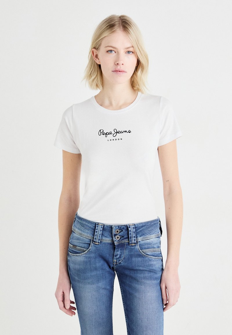 T-shirt en coton blanc à manches courtes, col rond, arborant un logo noir "Pepe Jeans London" sur la poitrine. Porté avec un jean en denim bleu.