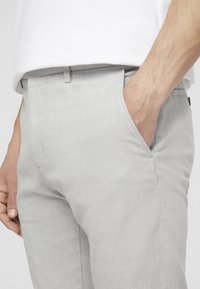 Light gray trousers with a textured surface. Features side pockets and a fitted waistband. Close-up view highlighting the fabric's pattern.