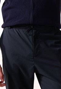 Pantalons bleu marine texturés avec un subtil éclat. Dispose d'une taille élastique avec un cordon de serrage, créant une coupe décontractée. Tissu lisse.