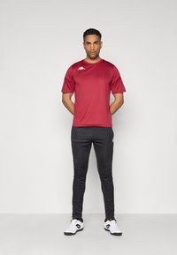 Rode sportieve T-shirt met korte mouwen, zwarte aansluitende broek en witte sportschoenen. Bevat logo-accenten op het shirt en de broek. Rekbaar materiaal, minimalistisch ontwerp.