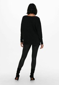 Czarny longsleeve z luźnym fasonem, sparowany z błyszczącymi czarnymi legginsami i czarnymi botkami na wysokim obcasie. Gładka tekstura, minimalistyczny design.
