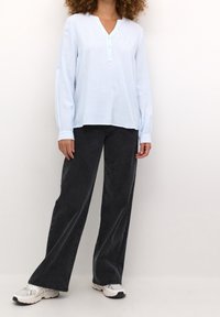 Chemise rayée bleu clair à manches longues avec un col Henley et des détails à boutons, associée à un jean large noir taille haute et des baskets blanches.