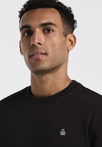 Zwarte katoenen sweatshirt met ronde hals en geribde manchetten, met een klein wit pinguïnlogo op de borst. Gladde textuur.