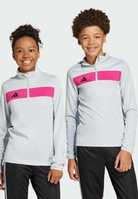 Witte lange mouwen sporttops met een gedurfde roze horizontale stripe, ritssluiting bij de kraag en zwarte accenten, gecombineerd met zwarte sportbroek.