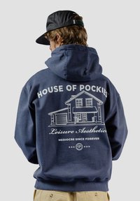 Sudadera azul marino con un gran gráfico blanco de una casa y el texto "HOUSE OF POCKIES" y "Leisure Aesthetics" en la parte de atrás. Textura suave, ajuste casual.