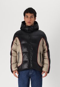 Casaco bomber com um corpo preto brilhante, painéis bege e detalhes vermelhos. Tem capuz, fecho na frente e dois bolsos laterais.