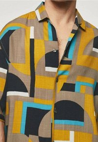 Camisa de manga corta en un tejido texturizado con patrones geométricos audaces en amarillo, azul, negro y blanco, con cierre de botones al frente.