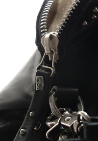 Sac en cuir noir avec fermeture éclair et quincaillerie en argent. Les caractéristiques incluent une étiquette marquée "A.S. 98" et des clous en métal le long des bords.