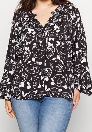 Sort bluse med lange ærmer med hvidt blomsterprint, V-hals og rynkede skulderdetaljer, båret sammen med lyseblå jeans.