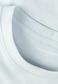 Κοντινή λήψη στον γιακά ενός λευκού T-shirt Jack & Jones με εμφανείς ραφές και εκτυπωμένη ετικέτα μεγέθους L/G, κατασκευασμένο στο Μπαγκλαντές.