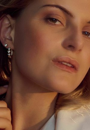 Guldringøreringe med funklende klare ædelsten, sammen med delikate hængende hjerteformede studs. Glat hudtekstur og blødt lys.