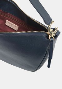 Marine leren handtas met een gestructureerde afwerking, gouden rits en een bordeauxrood gevoerd interieur met een label. Inclusief een verstelbare schouderriem.