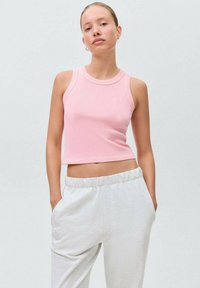 Svetlo roza rebrasti crop top s okroglim izrezom in brezrokavnim dizajnom, v kombinaciji s svetlo sivimi trenirka hlačami z elastičnim pasom.