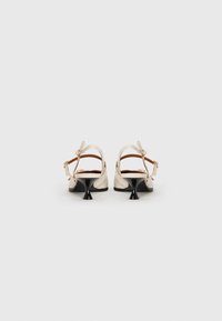 Pari kengät slingback beige, joissa on mustat korkeat kitten heels, näkyvä takaa taustalla valkoista.