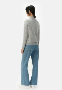 Grå stickad tröja med räfflade mudd och fåll, kombinerad med ljusblå vida denimjeans och vita sneakers, sedd bakifrån.