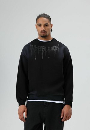 Zwarte sweatshirt met een gestructureerde "REBELLION" print in een druppelend ontwerp. Voorzien van een ronde hals en geribbelde manchetten, gecombineerd met donkere jeans.