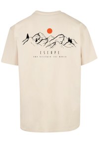 Beige cotton t-shirt featuring a mountain landscape graphic in black, with a red sun and the text "ESCAPE AND DISCOVER THE WORLD."