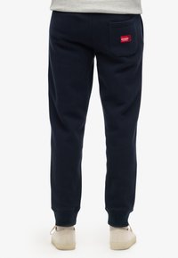 Marineblauwe katoenen joggingsbroeken met een ontspannen pasvorm, voorzien van cuffed hemlines, een achterzak en een klein rood merklabel.