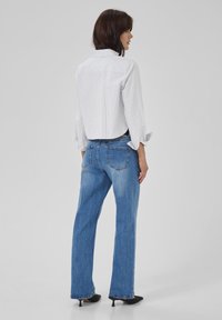 Camicetta bianca a righe, corta e con maniche lunghe, abbinata a jeans dritti azzurri chiari.Tacchi neri completano l'outfit.